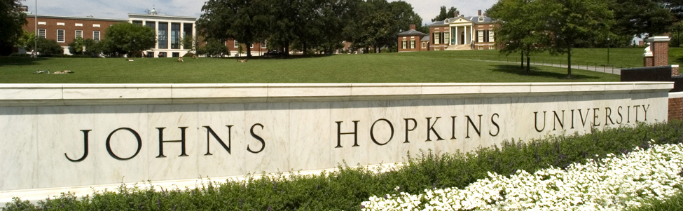 A sign welcoming visitors to Johns Hopkins University with the university library behind