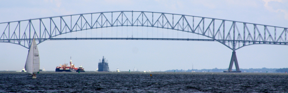 An arched bridge with two large ships in the background and a sailboat in the foreground